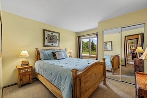 A bedroom with a large bed, two bedside tables with lamps, a large mirror, and a window with curtains.