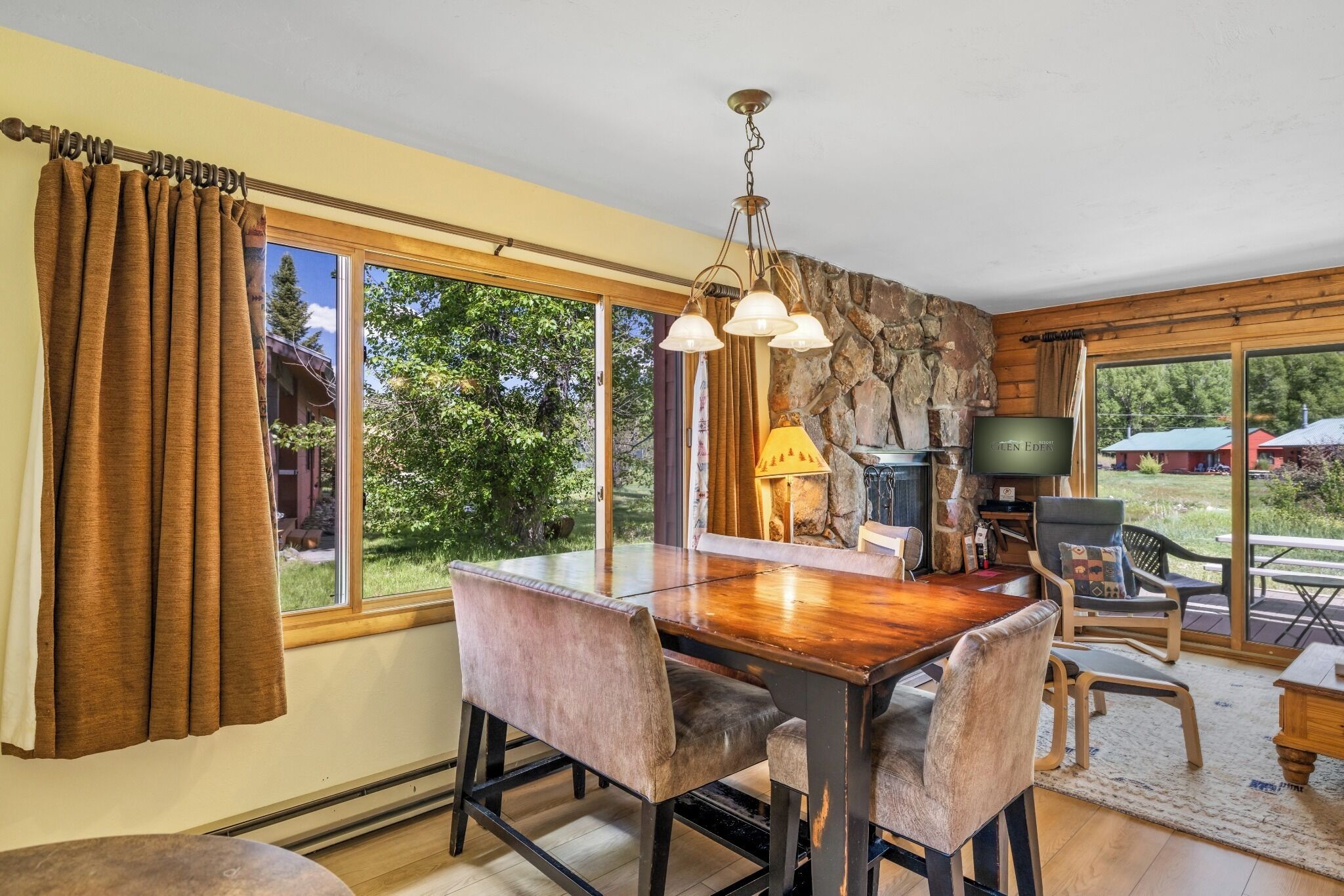 A dining area with a wooden table and chairs, a stone wall, and a television.