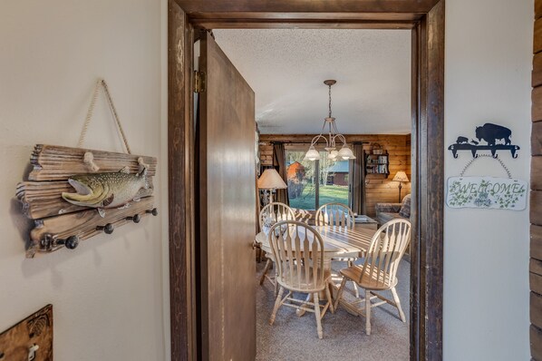 A wooden dining area with a table and chairs, a hanging light fixture, and a welcome sign with a buffalo silhouette. - Indian- Full kitchen, pet friendly, stunning views (Clark)