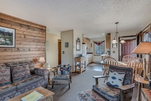 A cozy living room with a sofa, chairs, and a coffee table. There is a kitchen in the background with wooden cabinets and a dining table. - Indian- Full kitchen, pet friendly, stunning views (Clark)