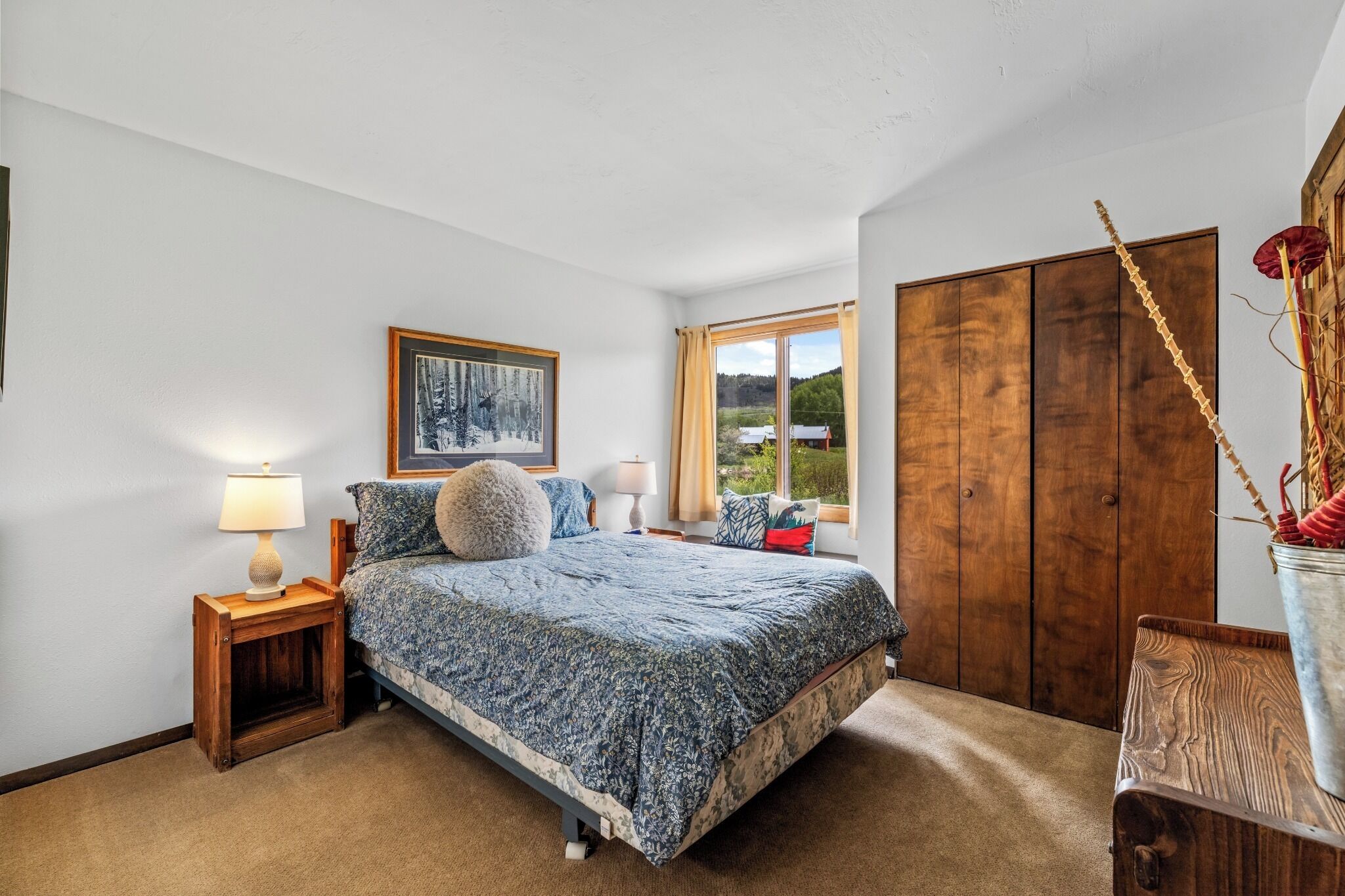 A bedroom with a bed, a nightstand, a window with a view, and a wardrobe.