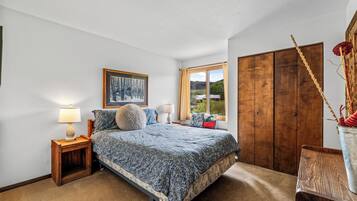A bedroom with a bed, a nightstand, a window with a view, and a wardrobe.