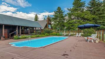 Un espace piscine doté d’une terrasse en bois, de chaises longues et d’un coin salon abrité.