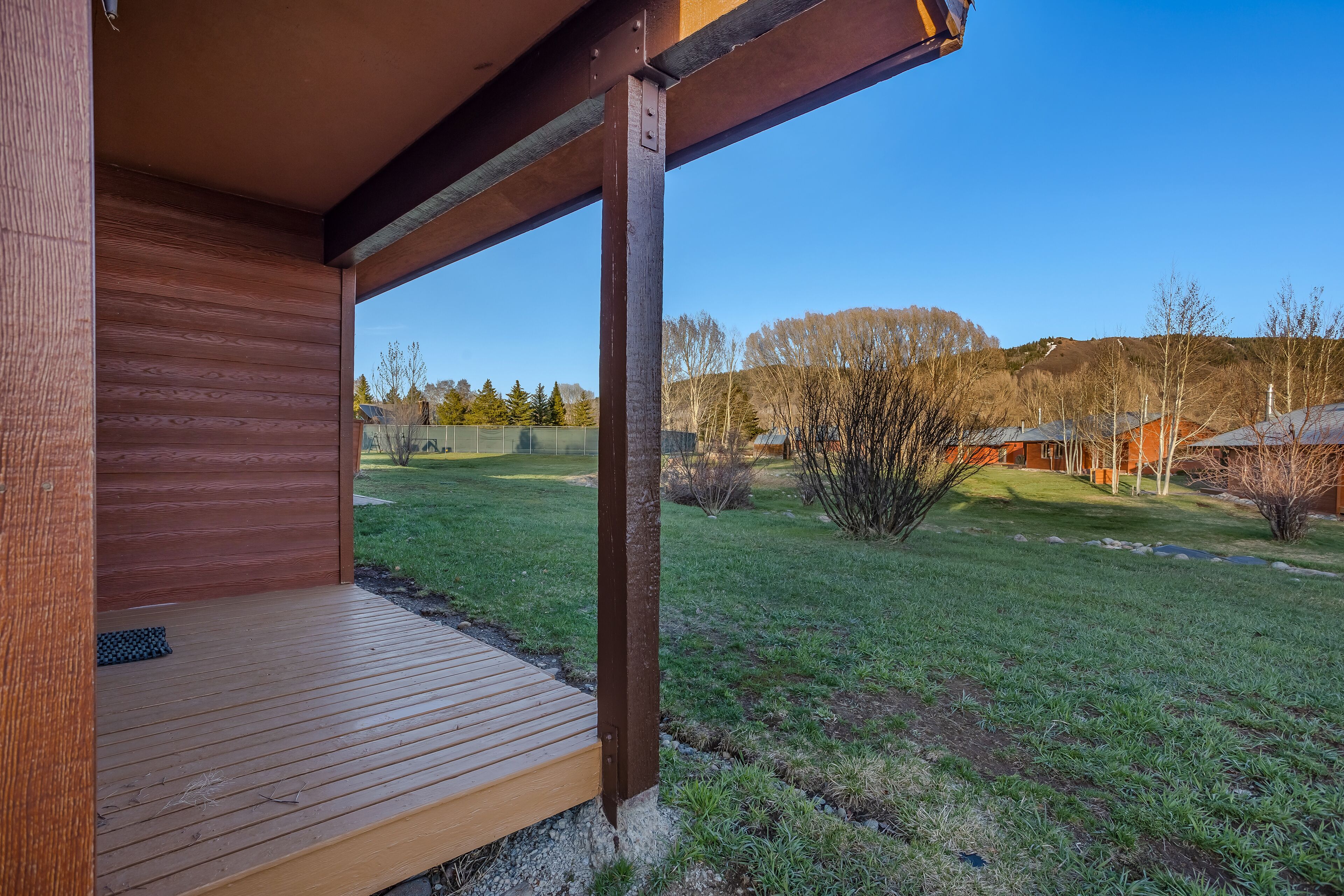 A wooden deck with a view of a grassy yard and distant trees.