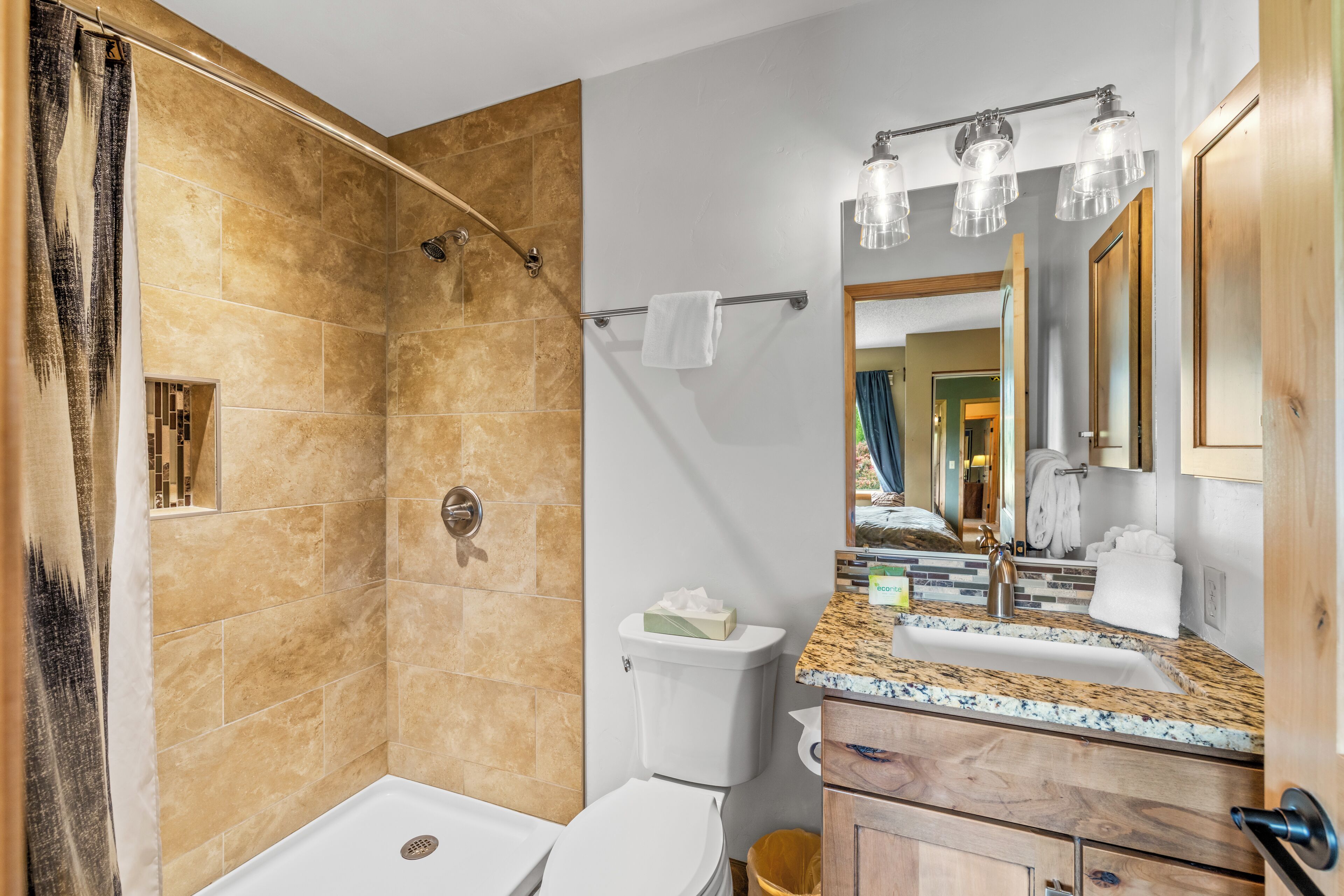 Une salle de bain équipée d’une douche, de toilettes, d’un lavabo et d’un miroir avec éclairage.