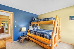 A bunk bed with a wooden frame, a bedside table with a lamp, and a blue wall. - Homesteader - Peaceful cabin with beautiful views (Clark)