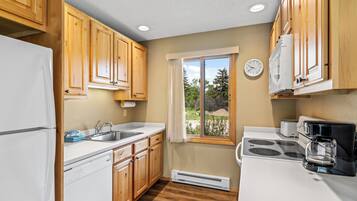 A kitchen with wooden cabinets, a white refrigerator, a stove, a sink, and a window with a view of trees.