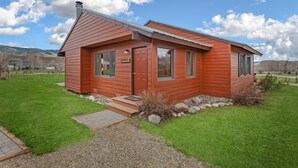 Une petite cabane en bois d’un seul étage, avec une porte rouge, de grandes fenêtres et un petit porche.