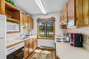 A compact kitchen with wooden cabinets, a microwave, a stove, and a window with a view of greenery.