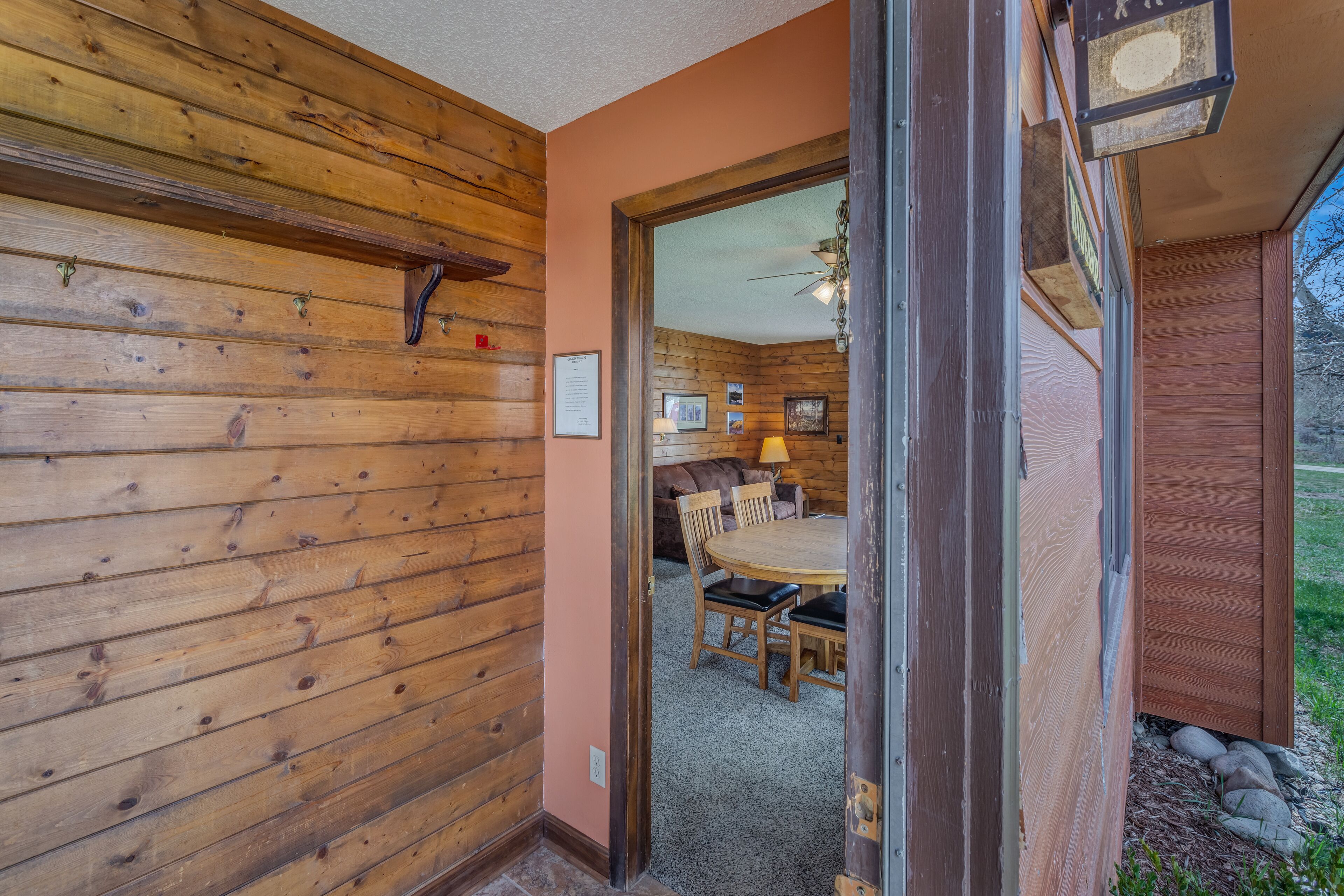 Un intérieur en bois comprenant un coin repas, un ventilateur de plafond et une vue sur l’extérieur par une porte ouverte.