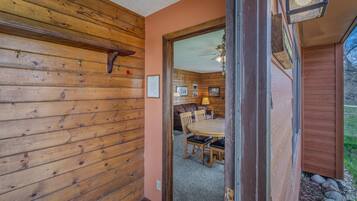 Un intérieur en bois comprenant un coin repas, un ventilateur de plafond et une vue sur l’extérieur par une porte ouverte.