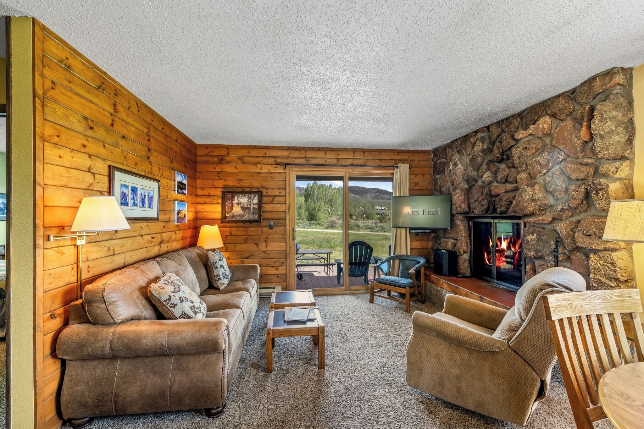A cozy living room with a stone fireplace, wooden walls, and a comfortable seating area.