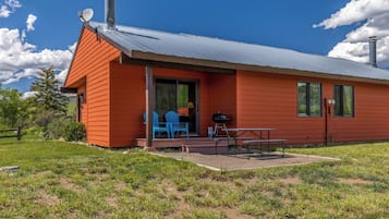 A single-story building with a red exterior, a covered patio area with a barbecue grill, and a blue chair.