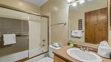 A bathroom with a bathtub, toilet, sink, and a large mirror.