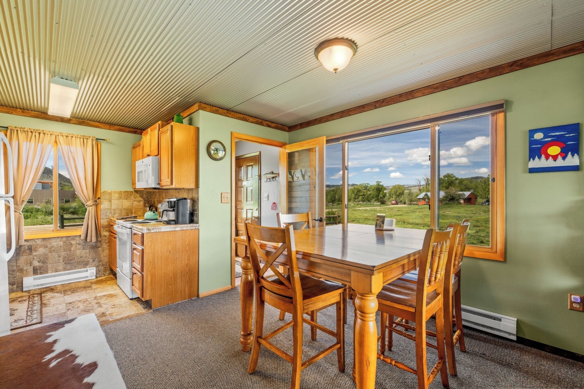A dining area with a table and chairs, a kitchen with wooden cabinets, and a view of the outdoors.