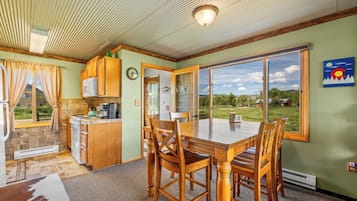 A dining area with a table and chairs, a kitchen with wooden cabinets, and a view of the outdoors.