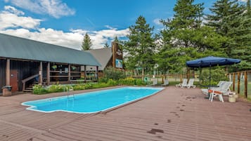 Ein Poolbereich mit Holzterrasse, Liegestühlen und einer überdachten Sitzecke.