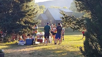 A group of people gathered around a table outdoors with a grassy field and trees in the background.