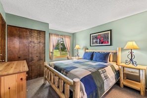 A bedroom with a wooden bed, a nightstand with a lamp, a wardrobe, and a window with curtains.