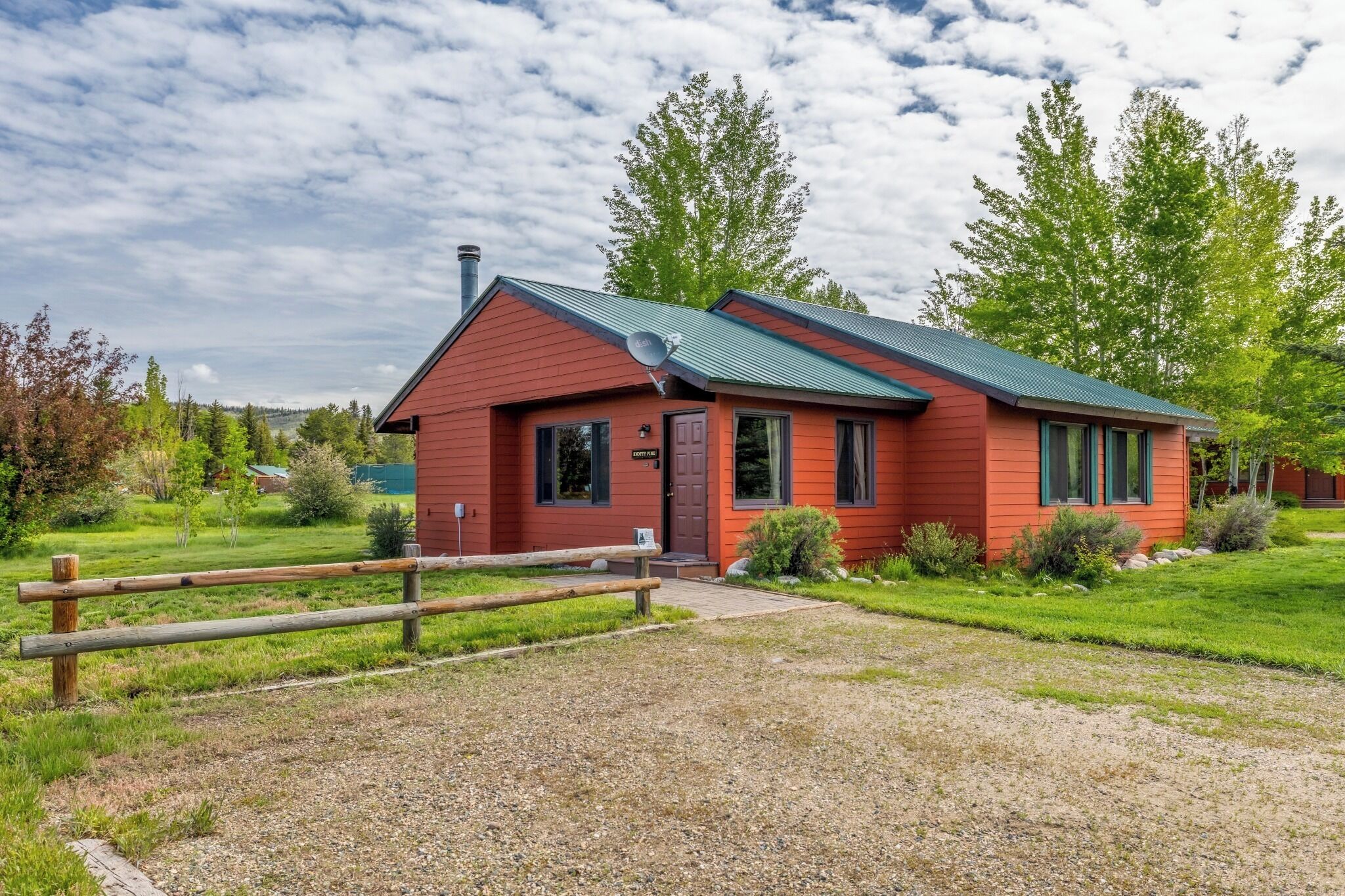A red building with a metal roof, a satellite dish, and a gravel driveway.