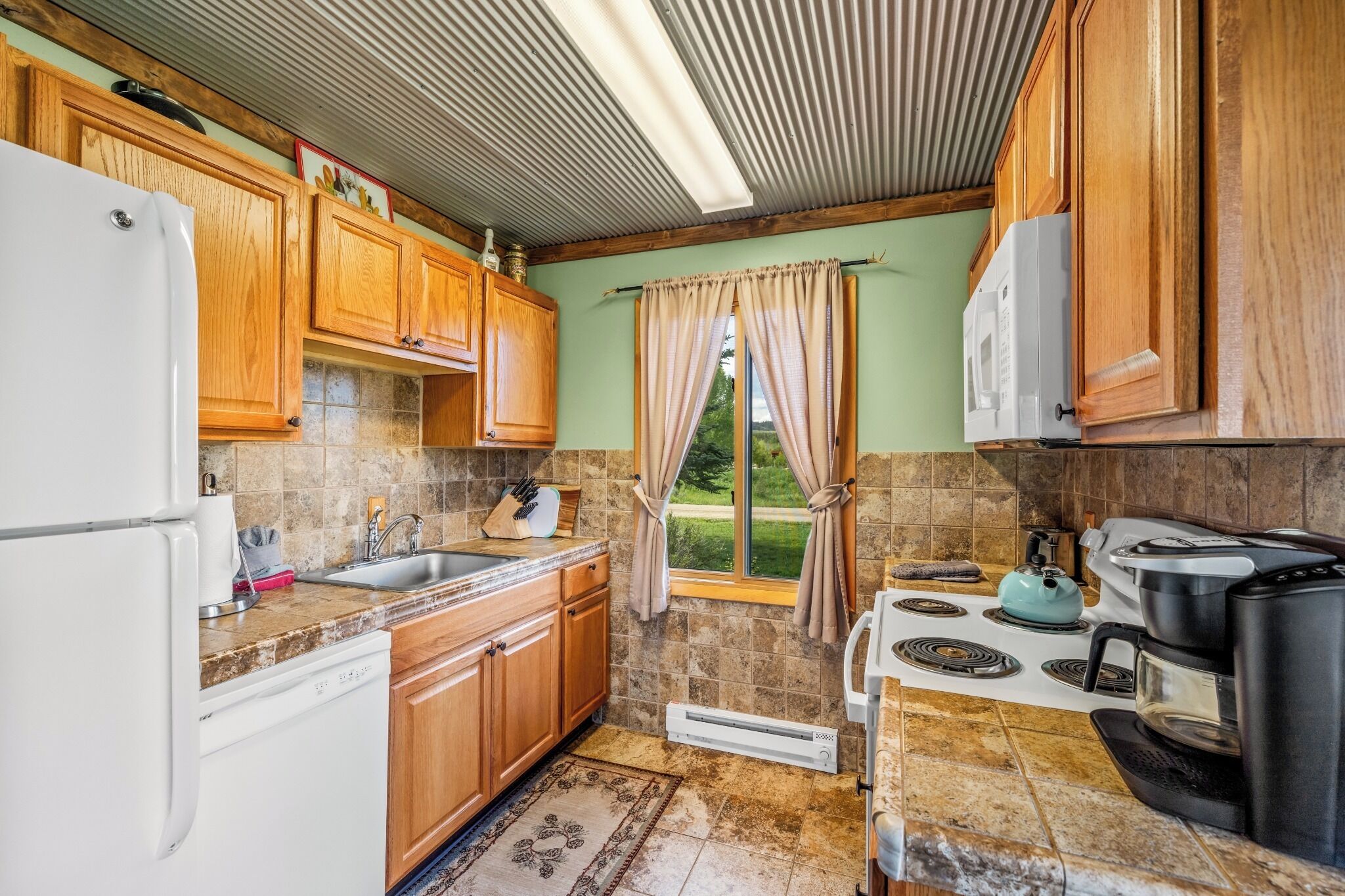 A kitchen with wooden cabinets, a white refrigerator, a sink, a stove, and a window with curtains.