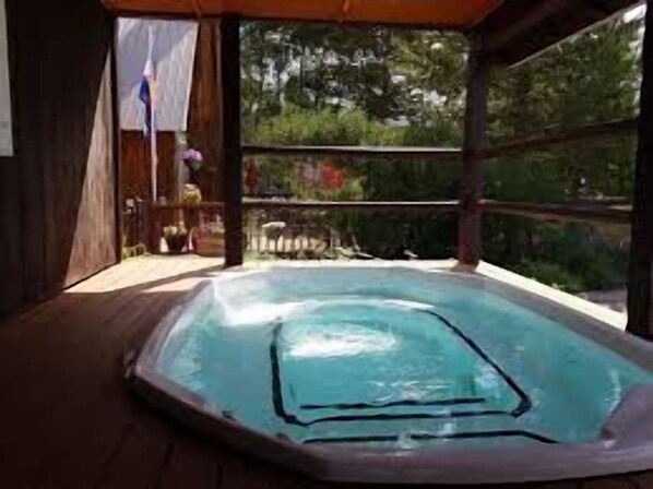 Un bain à remous situé dans un espace extérieur abrité, doté d’une terrasse en bois et offrant une vue sur les arbres et une clôture.