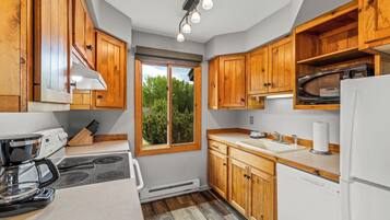 A compact kitchen with wooden cabinets, a built-in microwave, a coffee maker, and a window providing a view of greenery outside.