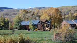 A rustic cabin with a metal roof, surrounded by a grassy field and autumn-colored trees. - Mustang - Escape to the wilderness (Clark)