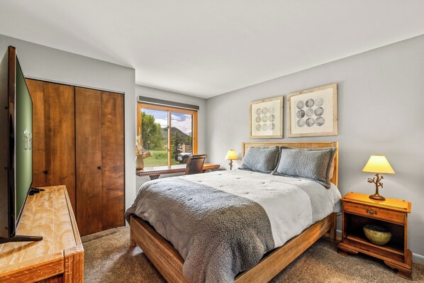 A bedroom with a wooden bed, two bedside tables with lamps, a window with a view, and two framed pictures on the wall. - Mustang - Escape to the wilderness (Clark)