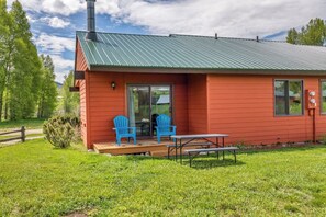 A red building with a metal roof, a sliding glass door, and a picnic table with two blue chairs. - Mustang - Escape to the wilderness (Clark)