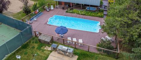 Une piscine rectangulaire avec une terrasse en bois, entourée d’une clôture, et un espace barbecue couvert.