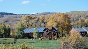A rustic cabin with a metal roof, surrounded by a grassy field and autumn-colored trees.
