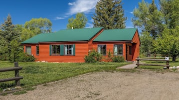 Une petite cabane à un seul étage, dotée d’un toit végétalisé, entourée d’une pelouse et d’arbres.