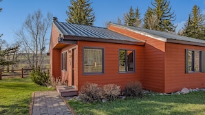 A single-story wooden cabin with a metal roof, a brick pathway leading to the entrance, and a small porch area. - Riverhouse - Fireplace, kitchen, pet friendly! (Clark)