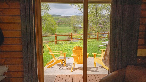 Une terrasse en bois avec des sièges d’extérieur, une vue sur un paysage verdoyant et une clôture en bois.