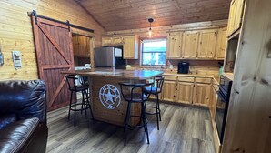 A cozy cabin-style kitchen with wooden cabinets, a central island with bar stools, and a sliding barn door. - Littlecreek: Rustic cabin get away. (Avinger)