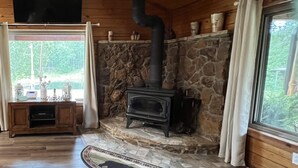 A cozy cabin interior with a stone fireplace, wooden walls, and a large window. - Littlecreek: Rustic cabin get away. (Avinger)