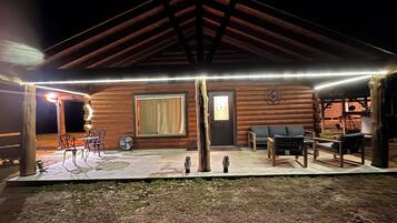 Una cabaña de troncos con un porche cubierto, amueblado con asientos exteriores y un ventilador.
