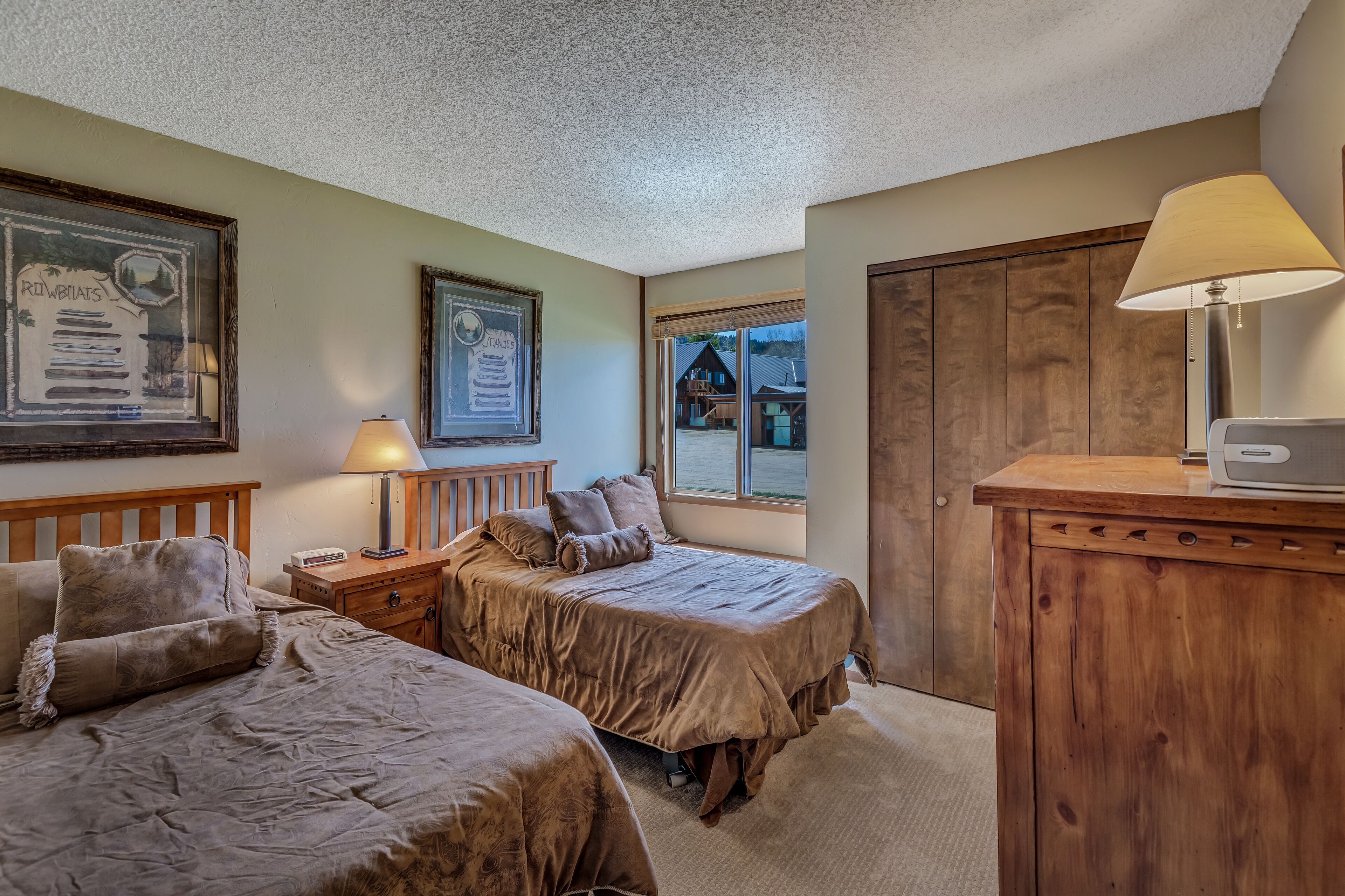 A bedroom with two beds, a wooden nightstand, a lamp, a dresser, and a framed picture on the wall.