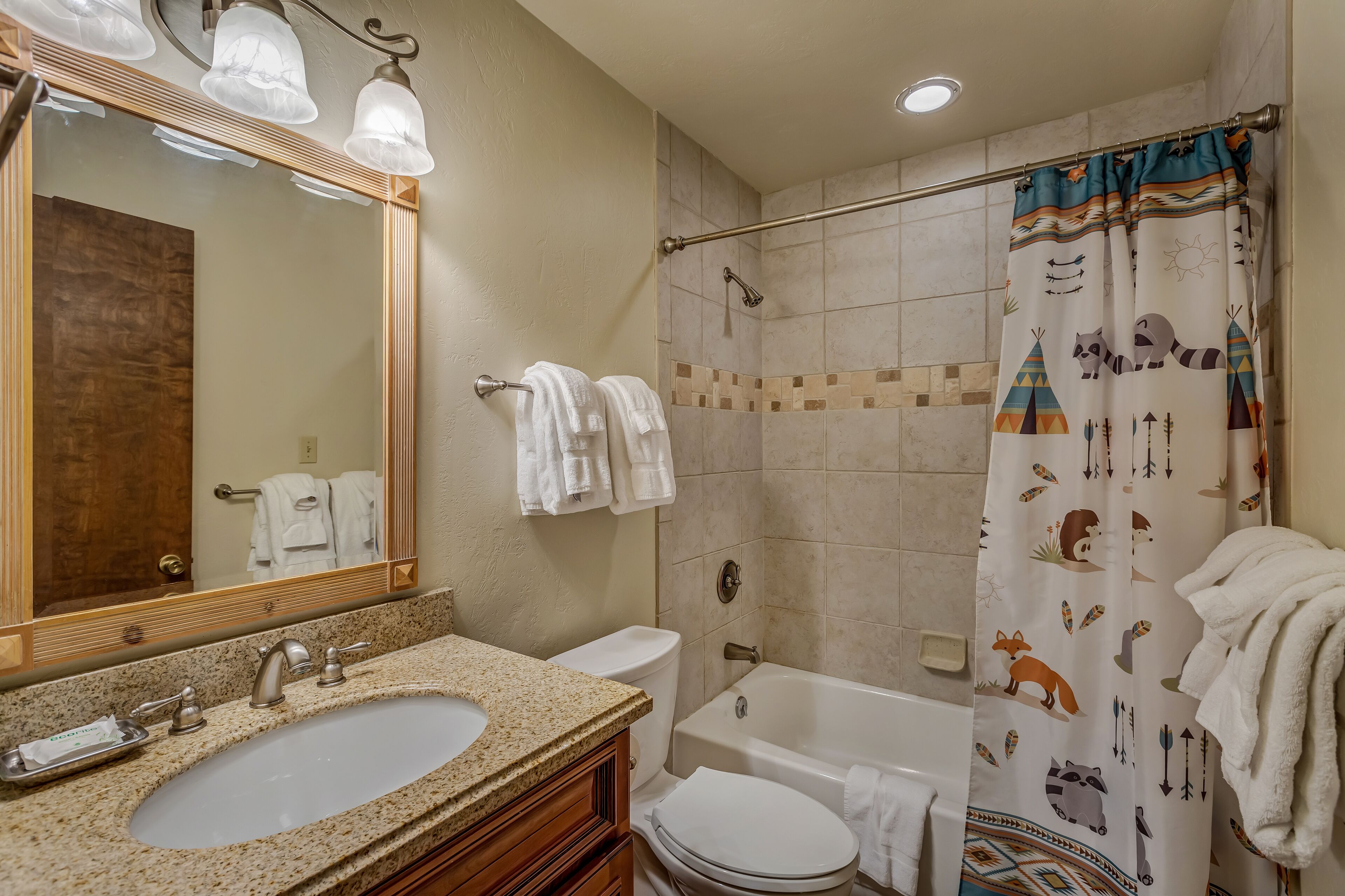 A bathroom with a sink, toilet, bathtub, and shower curtain with animal prints.