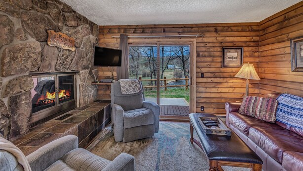 L’intérieur chaleureux d’un chalet avec une cheminée en pierre, un coin salon confortable et une grande fenêtre donnant sur le paysage extérieur.