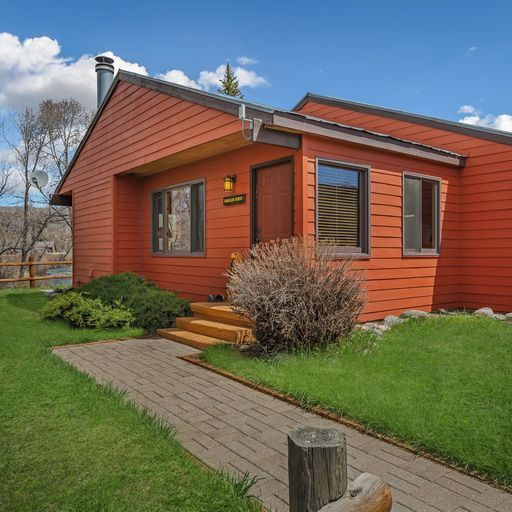 Une maison rouge à un étage, dotée d’un petit porche, d’une cheminée et d’une pelouse bien entretenue.