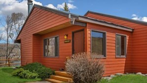 Une maison rouge à un étage, dotée d’un petit porche, d’une cheminée et d’une pelouse bien entretenue.