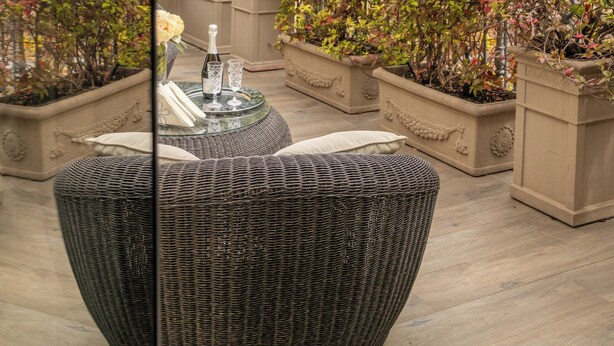 A rooftop terrace with potted plants, wicker furniture, and a view of historic buildings with domed roofs.