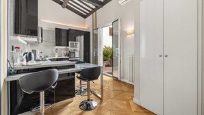 A modern kitchen with a central island, black bar stools, and a wooden herringbone floor.