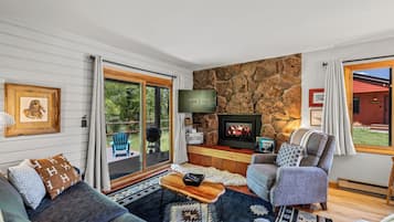 A cozy living room with a stone fireplace, comfortable seating, and a large window overlooking the outdoors.