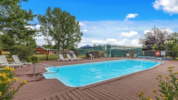 A swimming pool with a wooden deck, lounge chairs, and a fenced area with a lifebuoy.