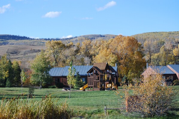 Eine rustikale Holzhütte mit Metalldach, umgeben von einem grasbewachsen Feld und herbstlich gefärbten Bäumen.