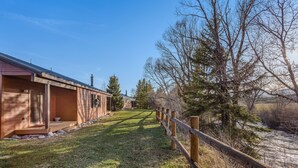 Un bâtiment moderne doté d’un espace extérieur couvert, d’une clôture en bois et, en arrière-plan, d’une rivière.