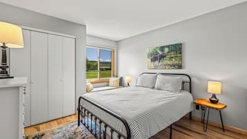 A bedroom with a bed, bedside lamps, a window with a view, a painting on the wall, and a wardrobe.